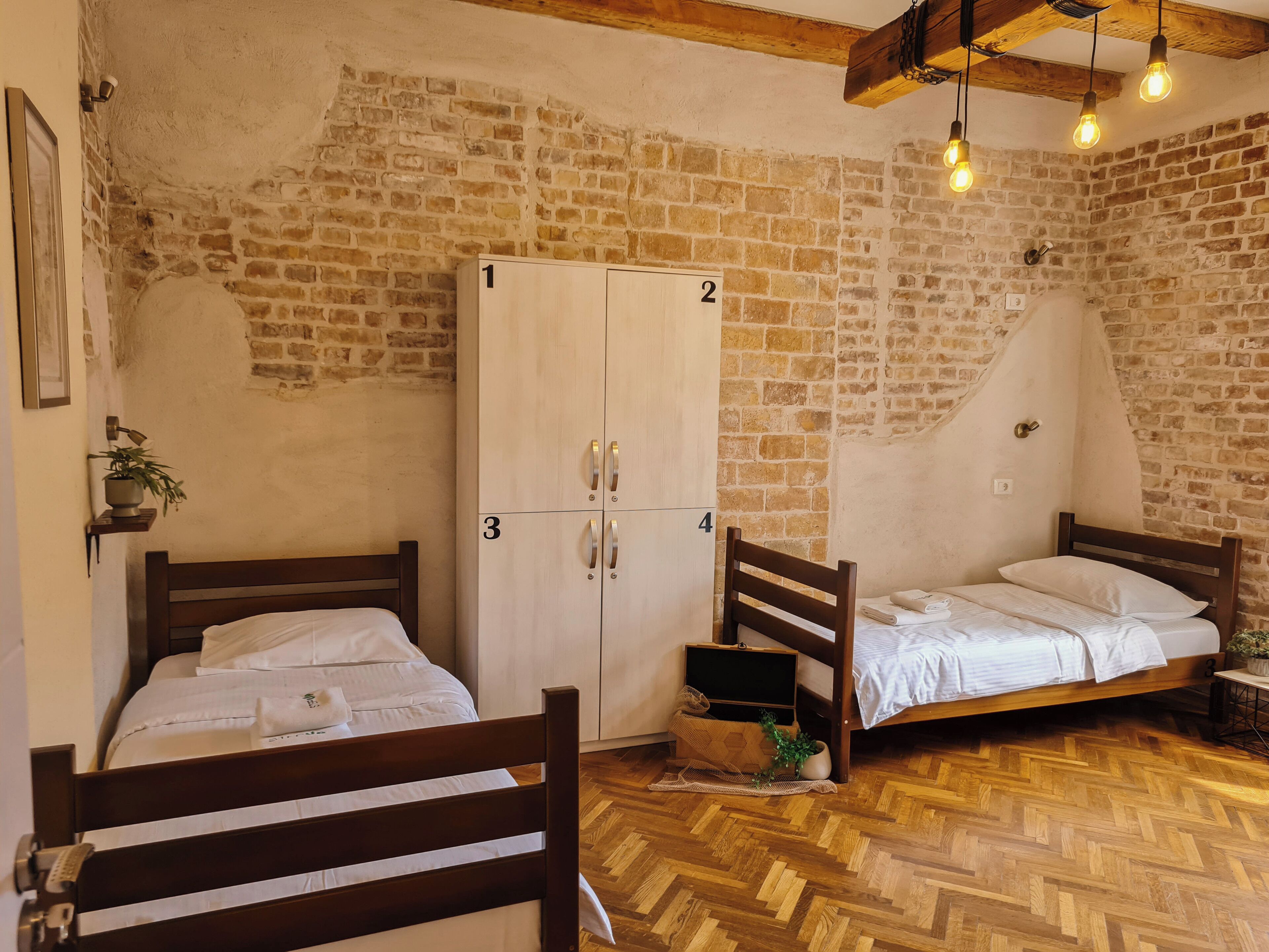 A room with two wooden beds, a wardrobe, and a brick wall.