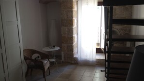 A small, dimly lit room with a stone wall, a wicker chair, a small round table, and a wooden bench. - JATTA - Beautiful Stone House Puglia (Conversano)