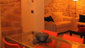 A modern living room with a glass dining table, red chairs, a sofa, and a stone accent wall. - JATTA - Beautiful Stone House Puglia (Conversano)