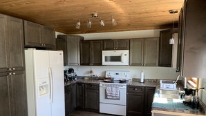 Une cuisine avec des meubles de rangement en bois foncé, un réfrigérateur blanc, un four à micro-ondes, une cuisinière et une machine à café.
