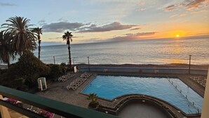 A pool area with lounge chairs and a view of the sunset over the ocean. - By the Beach & Pool Apartment (Funchal)