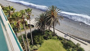A beach with a rocky shoreline, palm trees, and a view of the ocean. - By the Beach & Pool Apartment (Funchal)