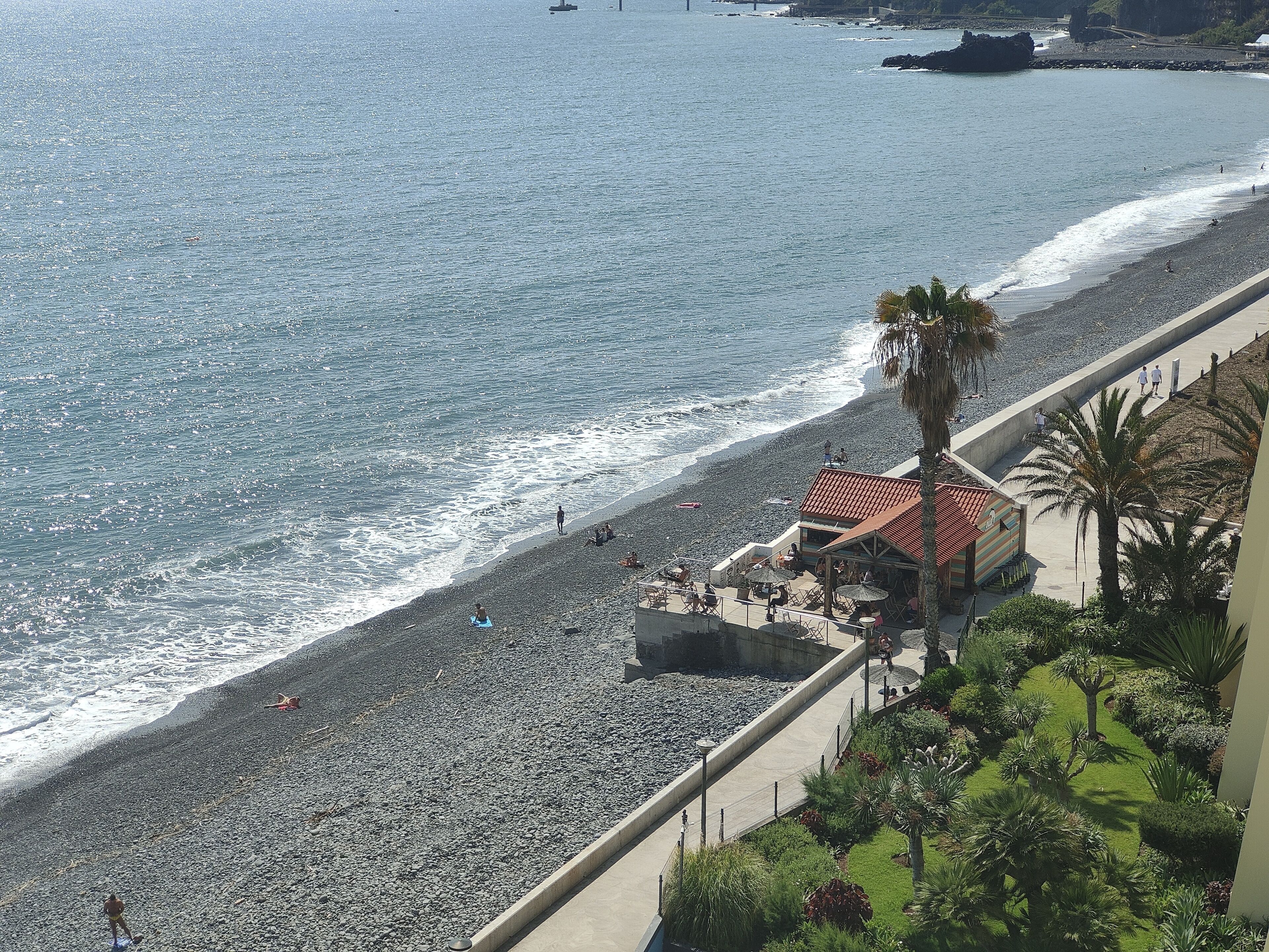 A beach with a building adjacent to it, featuring outdoor seating and a pathway.
