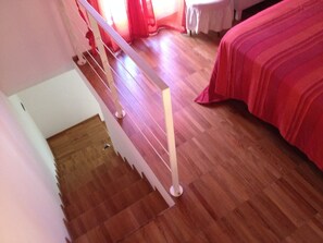 A staircase with a wooden floor leading to a room with a bed and a table.