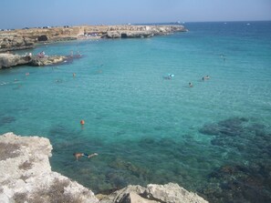 A coastal area with clear turquoise water, rocky formations, and people swimming and sunbathing.