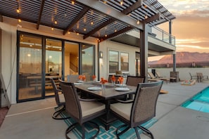 An outdoor dining area with a pool, covered patio, and mountain views.