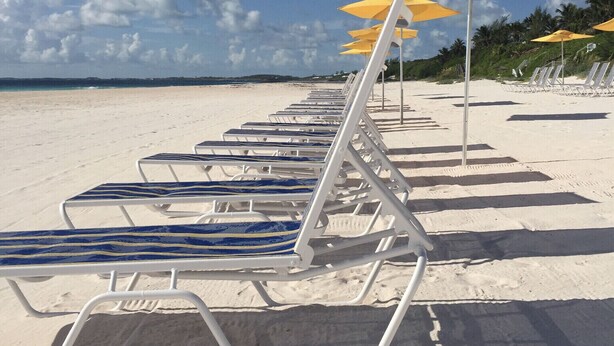 A beach with rows of white lounge chairs and yellow umbrellas. - Malda House (Dunmore Town)