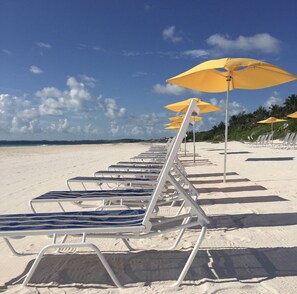A beach with rows of white lounge chairs and yellow umbrellas. - Malda House (Dunmore Town)