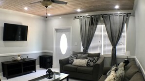 A living room with a ceiling fan, a flat-screen TV, a sofa, a coffee table, and a window with curtains. - Malda House (Dunmore Town)