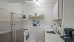 Una cocina compacta con un refrigerador de acero inoxidable, una estufa a gas y una cafetera.