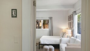 Un dormitorio con cama, sofá, ventana con cortinas y lámpara de noche.