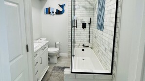A modern bathroom with a glass-enclosed shower, a white bathtub, and a marble backsplash.