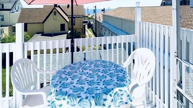 A deck with a round table and two chairs, a red umbrella, and a white fence.