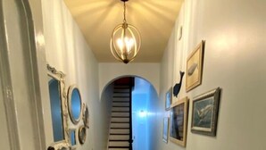 A hallway with wooden flooring, white walls, and a staircase leading to another room.
