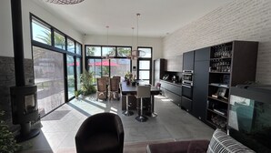 A modern kitchen with large windows, a dining area, and a built-in bookshelf. - New house, Jacuzzi, Terrace, Near to Beaches and Shops (Le Tour-du-Parc)
