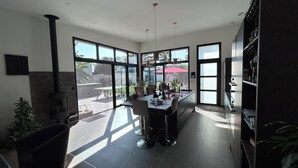 A modern kitchen with large windows, a dining area with bar stools, and a view of the outdoor patio. - New house, Jacuzzi, Terrace, Near to Beaches and Shops (Le Tour-du-Parc)