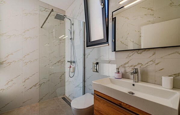 Un baño moderno con cabina de ducha de vidrio, un lavamanos blanco y un espejo sobre el lavamanos.