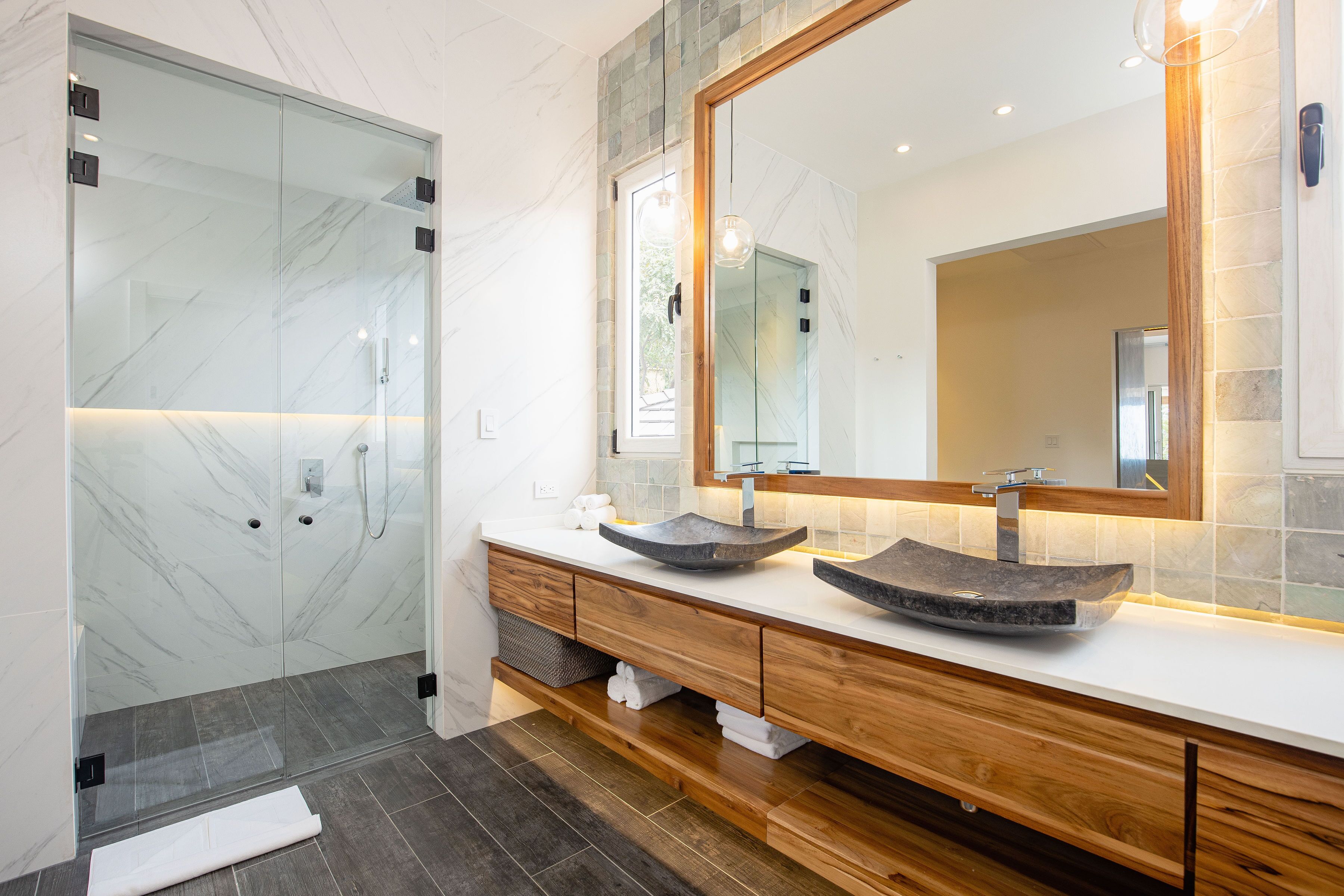A modern bathroom with a glass shower enclosure, a wooden vanity with two vessel sinks, and a large mirror above the vanity.