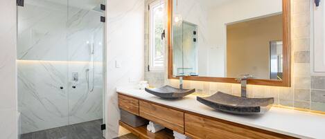 A modern bathroom with a glass shower enclosure, a wooden vanity with two vessel sinks, and a large mirror above the vanity.