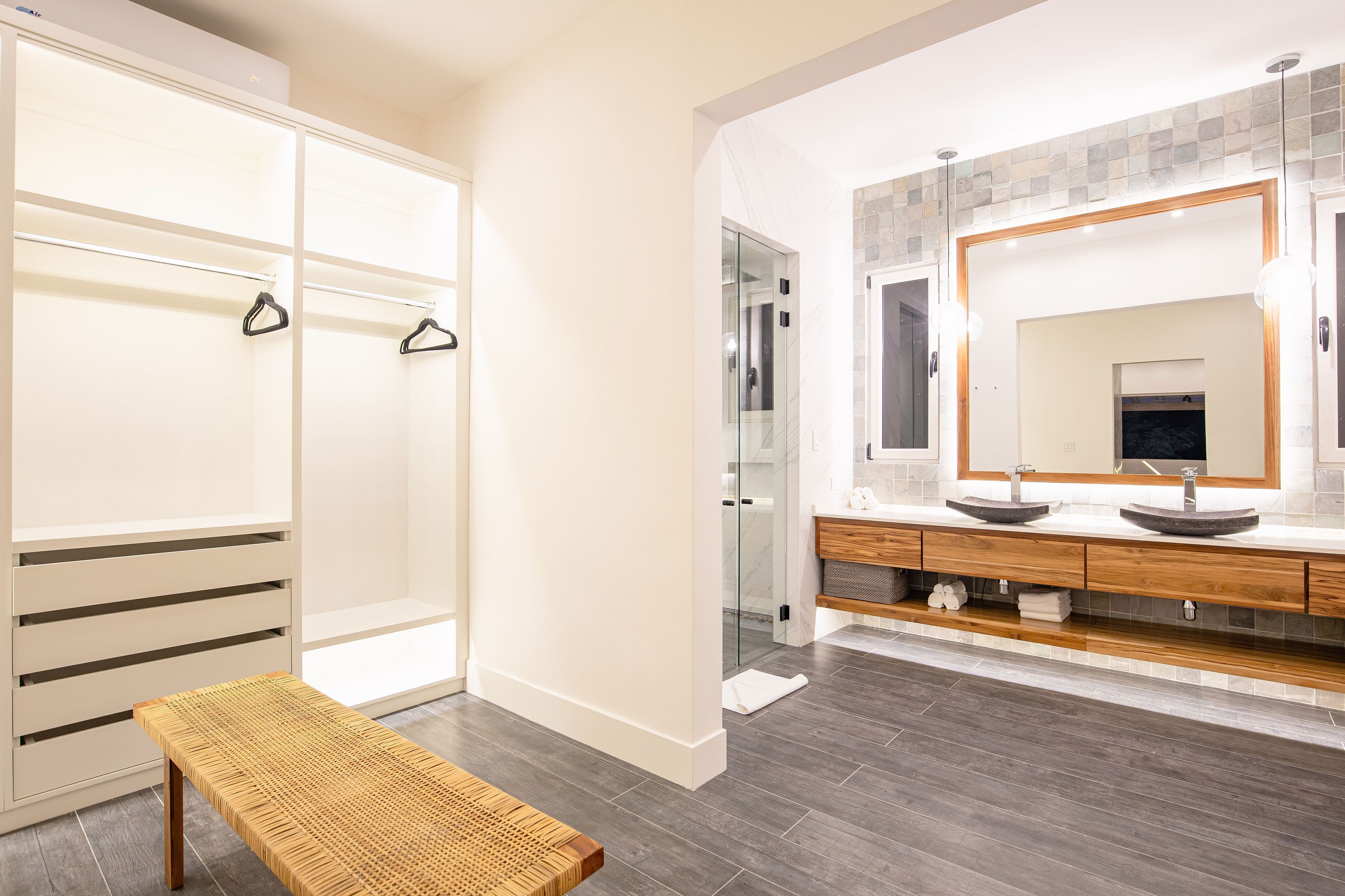 A modern bathroom with a large mirror, two sinks, and a bench.