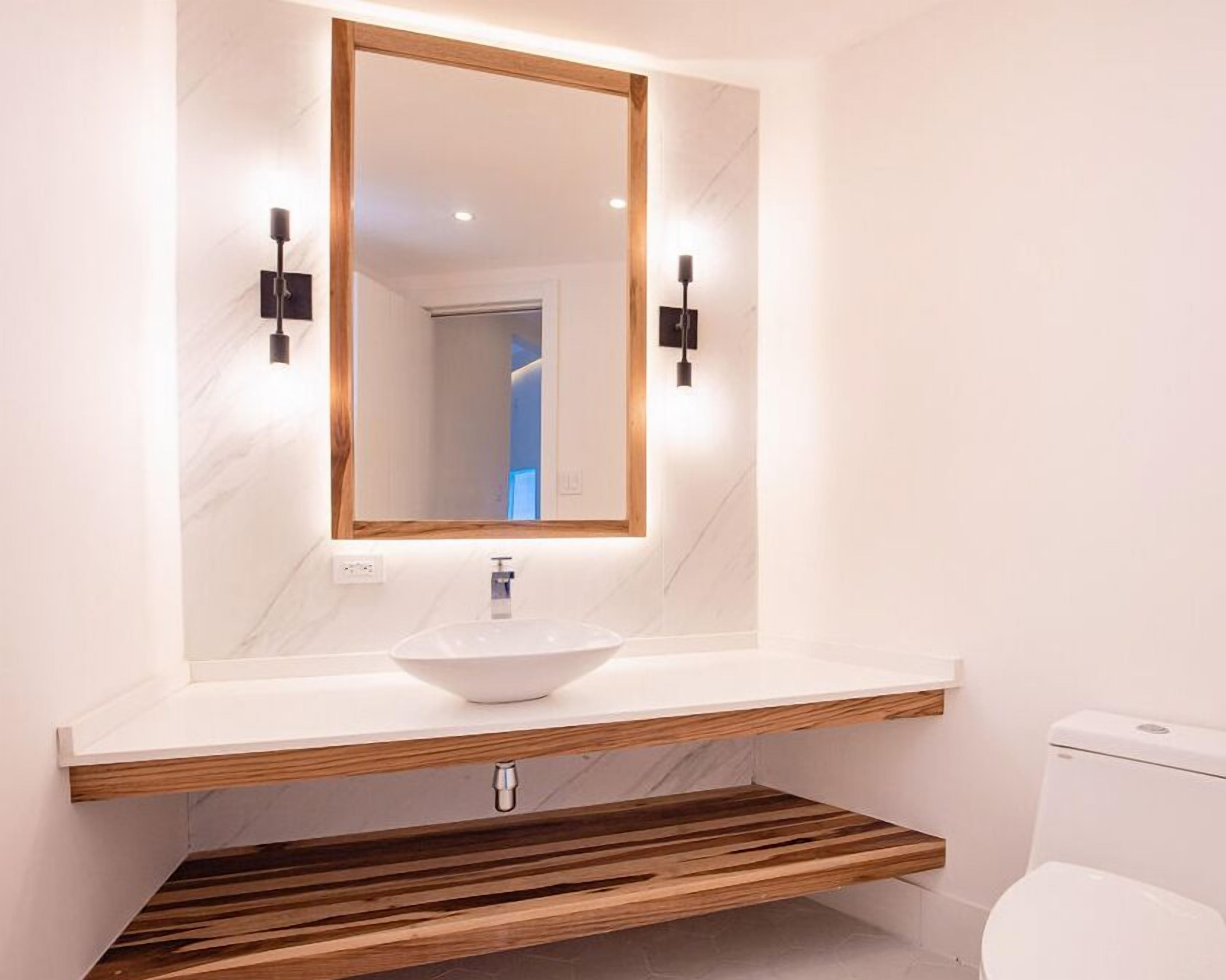 Un baño moderno con lavamanos de mármol blanco, tocador de madera y un espejo grande.