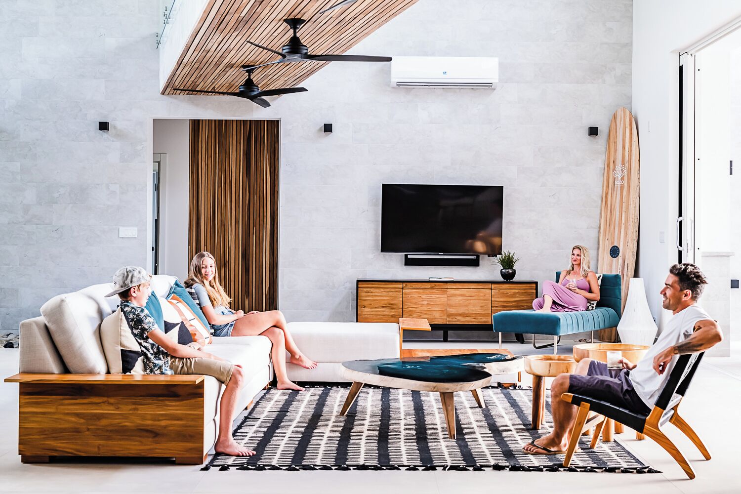 Ein modernes Wohnzimmer mit großem Flachbildfernseher, Holzboden und einem großen Fenster mit Vorhängen.