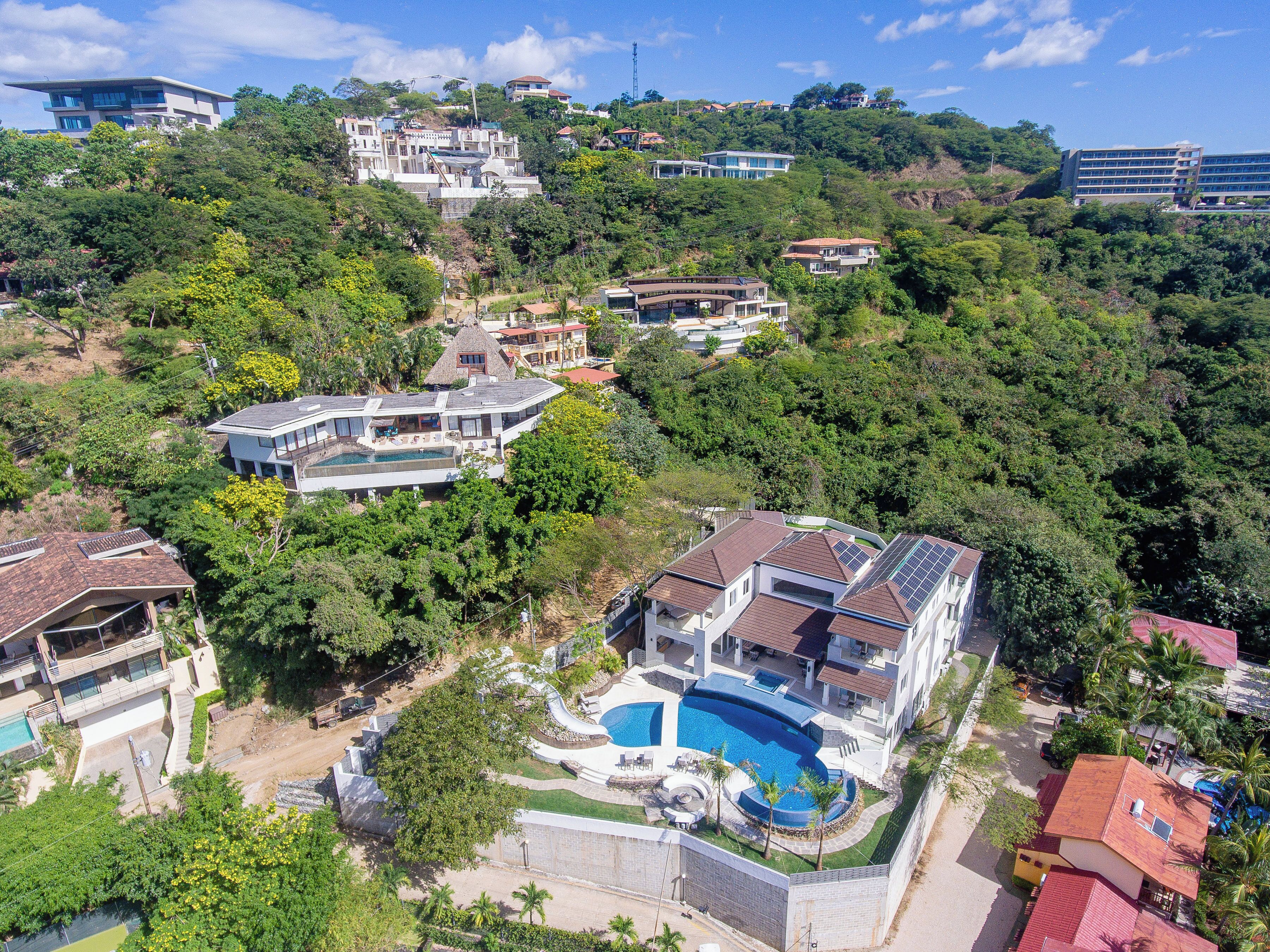 Una zona residencial en una ladera con varias casas, una piscina grande y abundante vegetación.