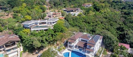 Una zona residencial en una ladera con varias casas, una piscina grande y abundante vegetación.