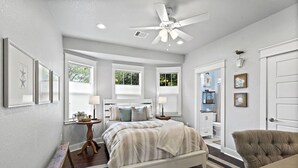 A bedroom with a bed, bedside tables, a ceiling fan, and a view of the outdoors.