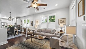 A spacious living room with a ceiling fan, a dining area with a table and chairs, and a kitchen in the background.