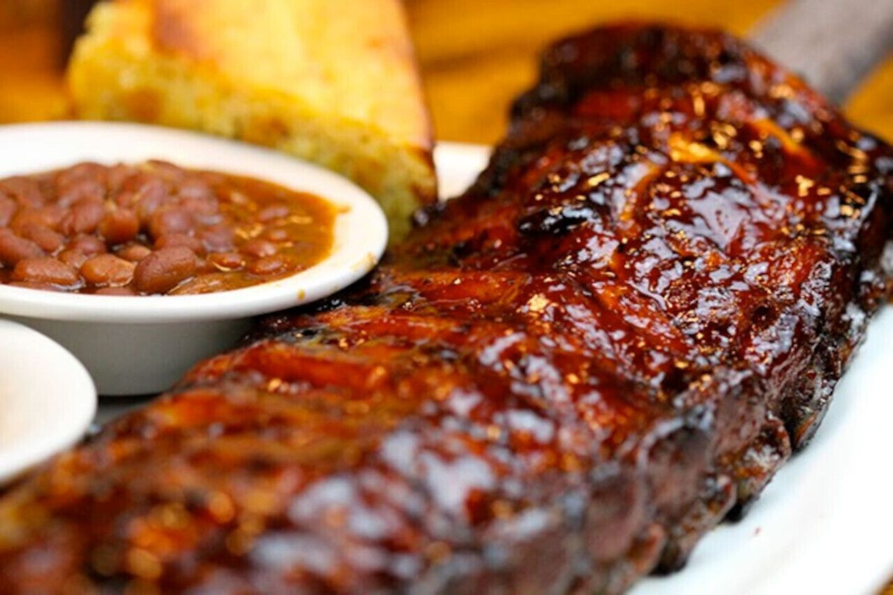 A plate of barbecued ribs with a side of baked beans and cornbread.