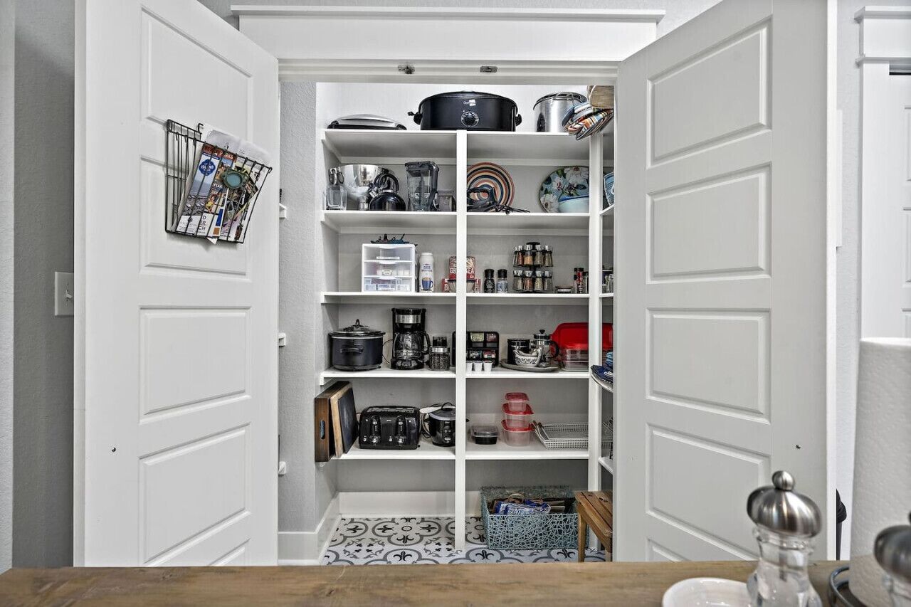 A kitchen pantry with white doors, shelves stocked with kitchenware, and a tiled backsplash.
