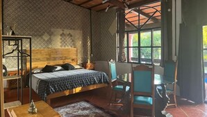 A room with a bed, a table, and chairs, a ceiling fan, and a window with a view of greenery. - Hospedaje Los Cruxes Tepoztlan (Tepoztlán)