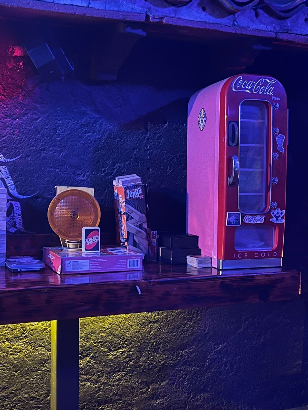 Una máquina expendedora vintage de Coca-Cola, cartas de UNO y cajas de Jenga sobre una mesa de madera.
