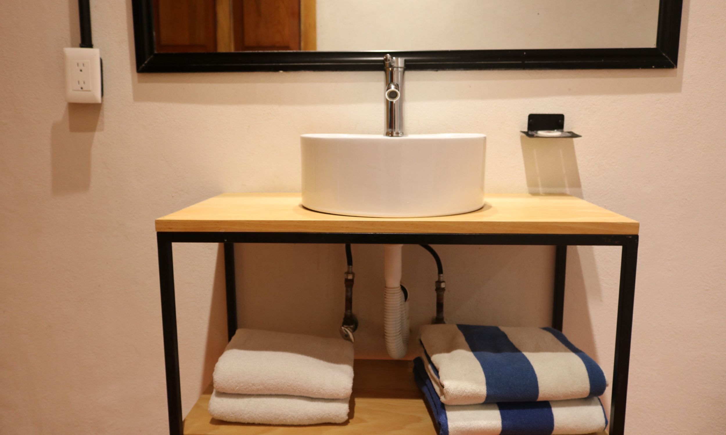 A bathroom with a white sink, a mirror, a towel rack, and a towel dispenser.