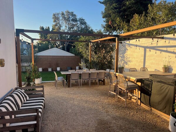 An outdoor patio with a wooden table and chairs, a covered seating area, and a brick wall.