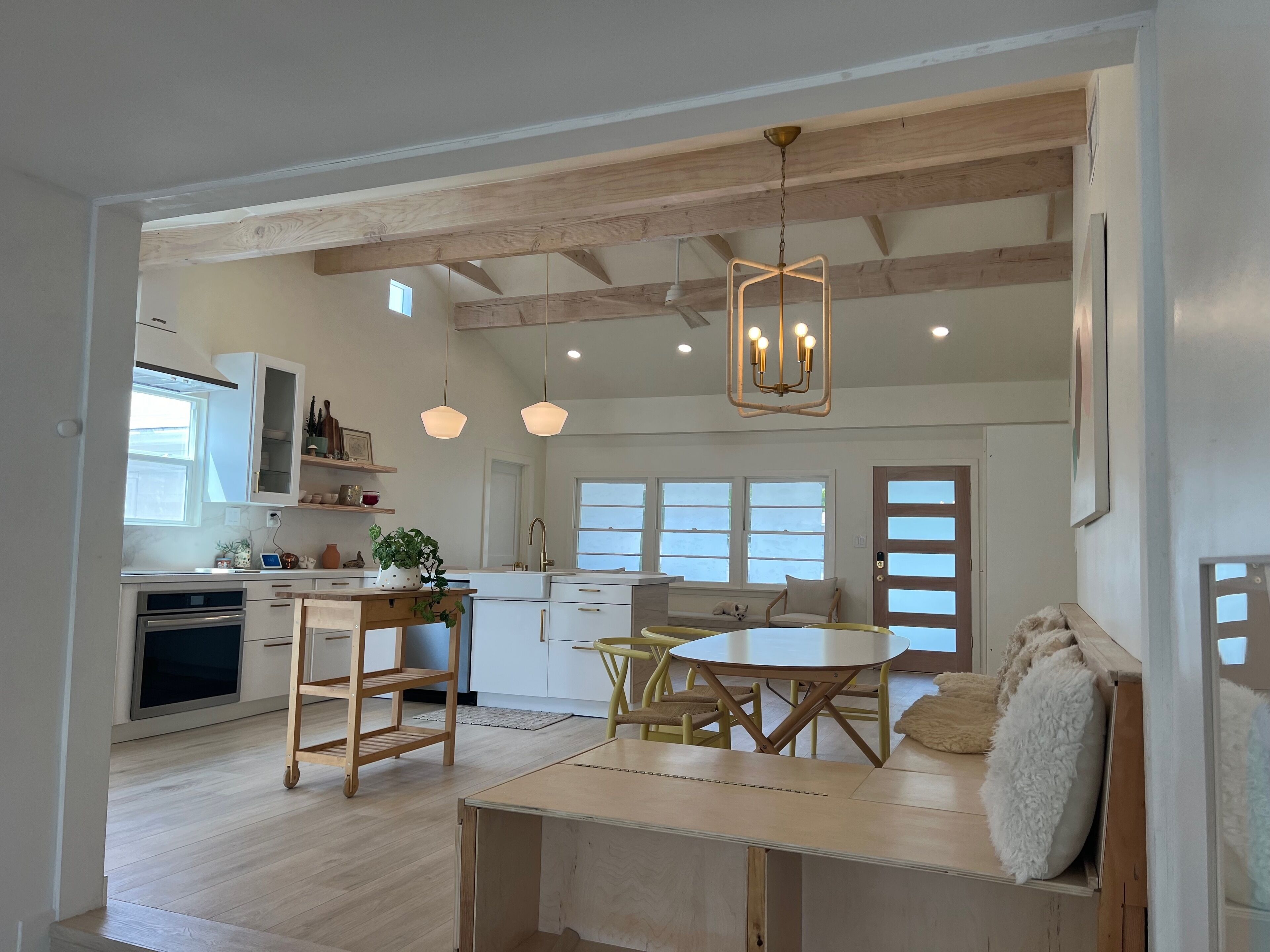 Une cuisine moderne avec des poutres en bois, un coin repas avec une table et des chaises, et un espace salon confortable avec un canapé et des coussins.