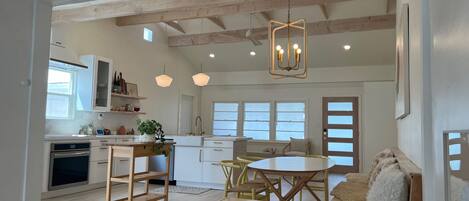 A modern kitchen with wooden beams, a dining area with a table and chairs, and a cozy seating area with a sofa and cushions.