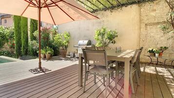 Eine Holzterrasse mit Tisch, Stühlen, einem Grill und Topfpflanzen.