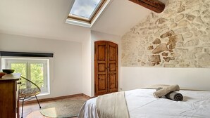 A bedroom with a stone wall, a skylight, a wooden wardrobe, and a bed with pillows. - Le 115, air-conditioned town house with interior courtyard and swimming pool (Pernes-les-Fontaines)
