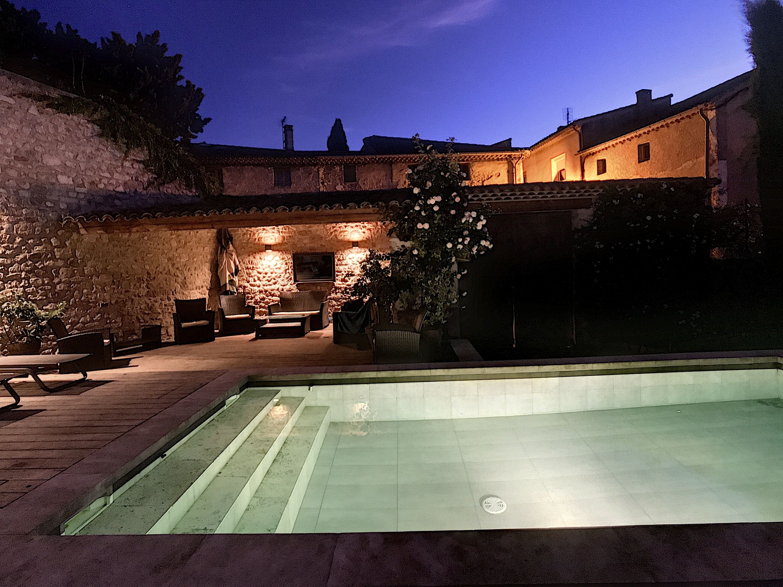 Ein Poolbereich mit Steinmauern, Gartenmöbeln und einer gut beleuchteten Terrasse.