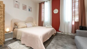 Un dormitorio con cama, mesita de noche, lámpara, espejo y ventana con cortinas.