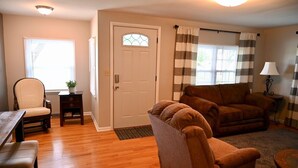 Een woonkamer met een houten vloer, een beige fauteuil, een bruine bank, een eettafel met stoelen en een deur met een raam.