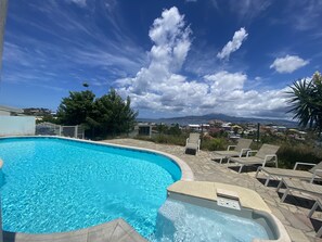 A swimming pool with a hot tub, surrounded by lounge chairs and a scenic view of a coastal town. - Ti Mélissa - Swimming Pool, Ocean View, Parking (Trois-Ilets)