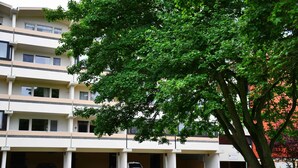 A multi-story building with a parking garage, green trees, and a clear sky.