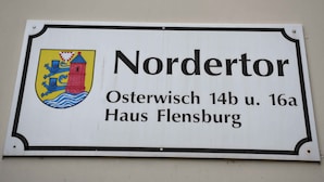 Una señal con el nombre 'Nordertor' y la dirección 'Osterwisch 14b u. 16a Haus Flensburg'.
