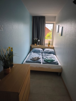 Un dormitorio pequeño y ordenado con una cama individual, una mesita de noche con lámpara y una ventana con cortinas.
