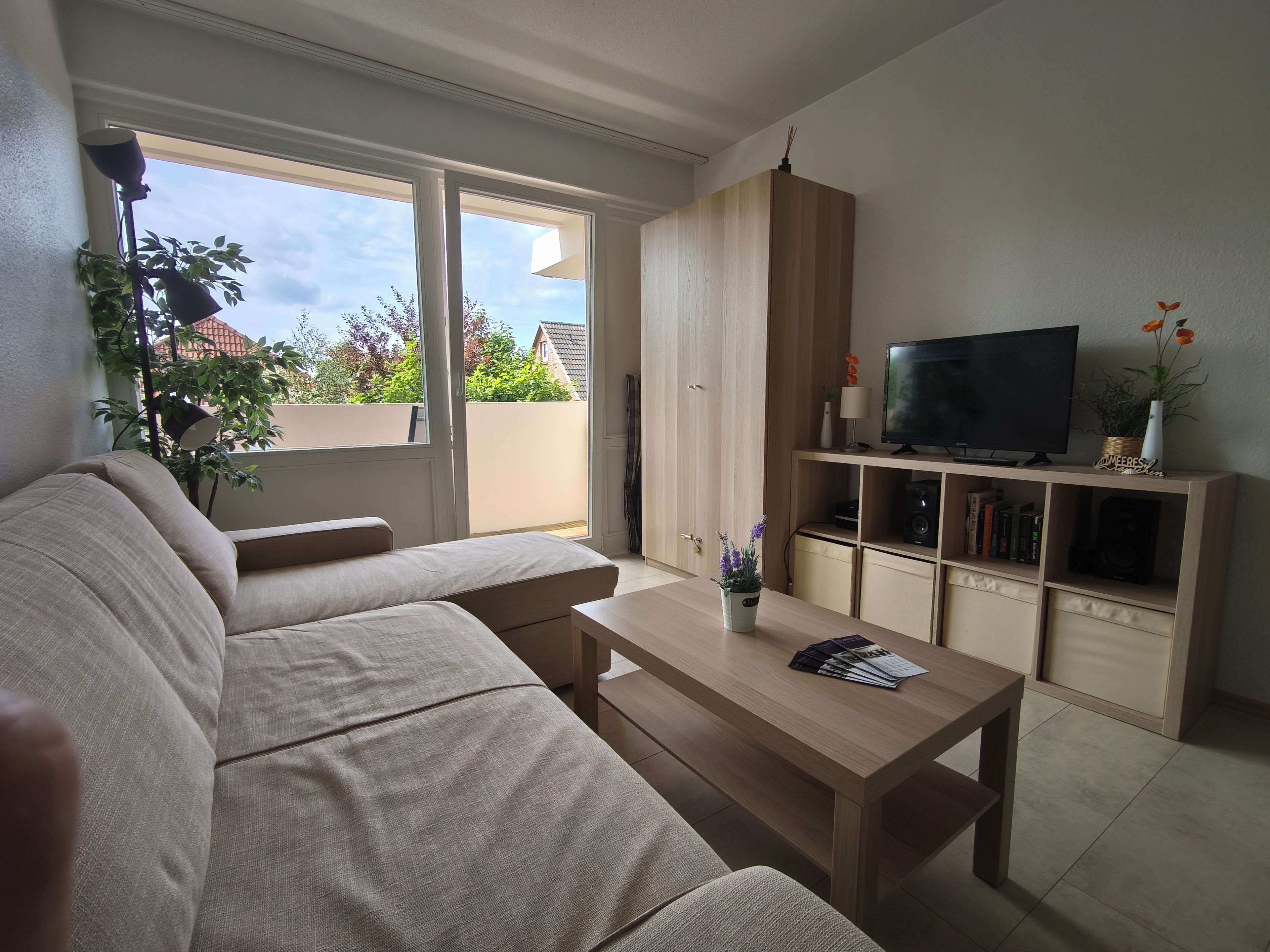 Una sala de estar con un sofá, una mesa de centro, un televisor sobre un mueble de madera y una estantería.