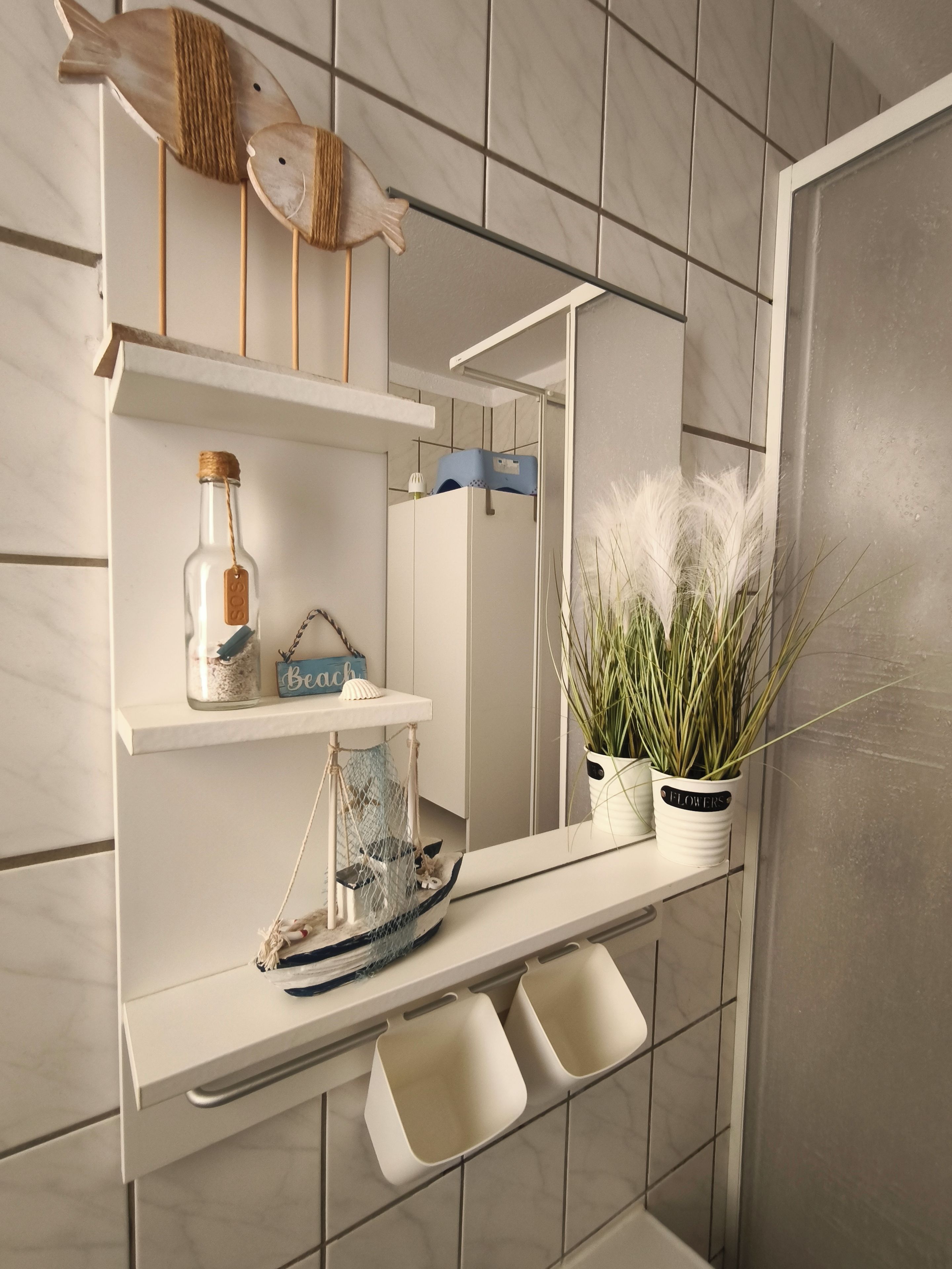 Een badkamer met een wit wastafelmeubel, een spiegel, een plank met decoratieve objecten en een potplant.