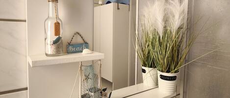 Een badkamer met een wit wastafelmeubel, een spiegel, een plank met decoratieve objecten en een potplant.